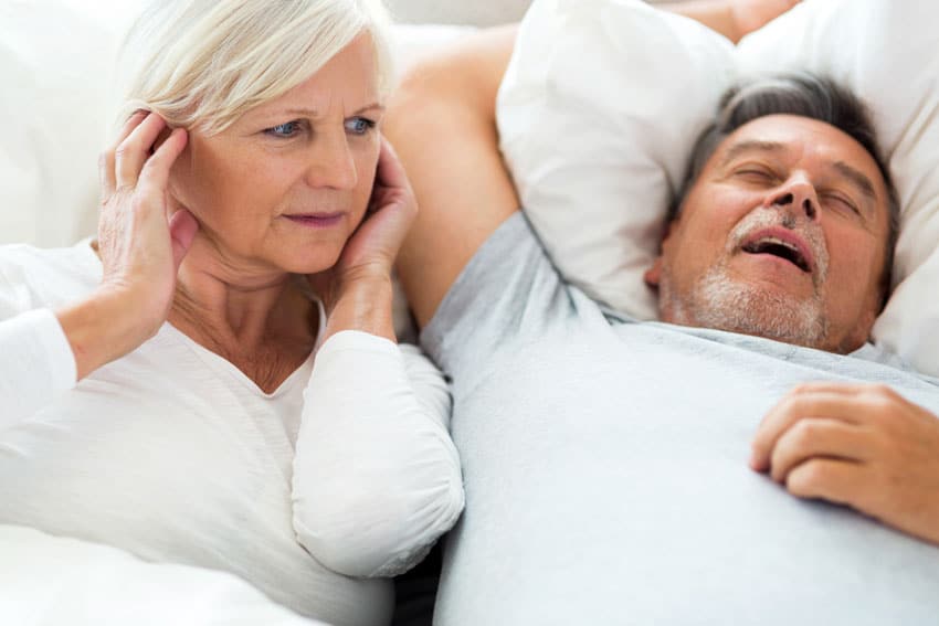 senior man snoring while partner plugs her ears